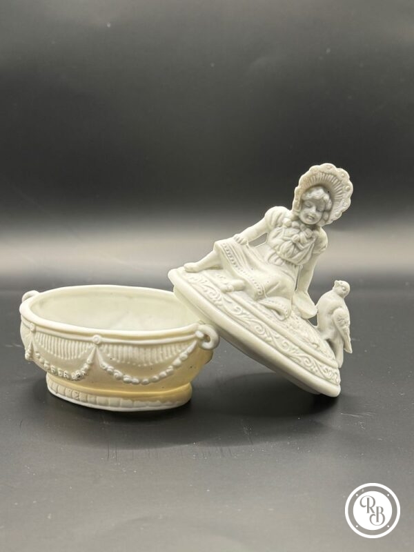bonbonnière en biscuit (boite à bijoux) avec personnage et oiseau sur le couvercle.