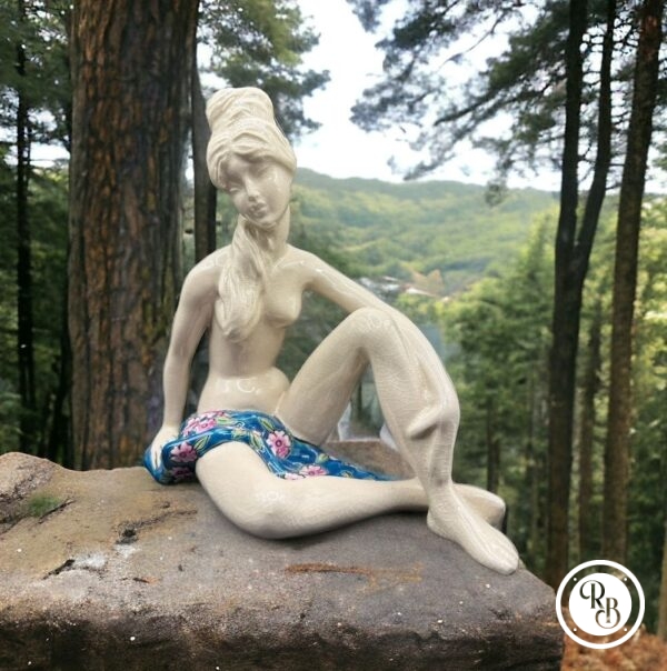 Sujet en céramique craquelée et émaillée figurant une jeune femme nue et assise, partiellement couverte d'une serviette à décor de fleurs polychromes