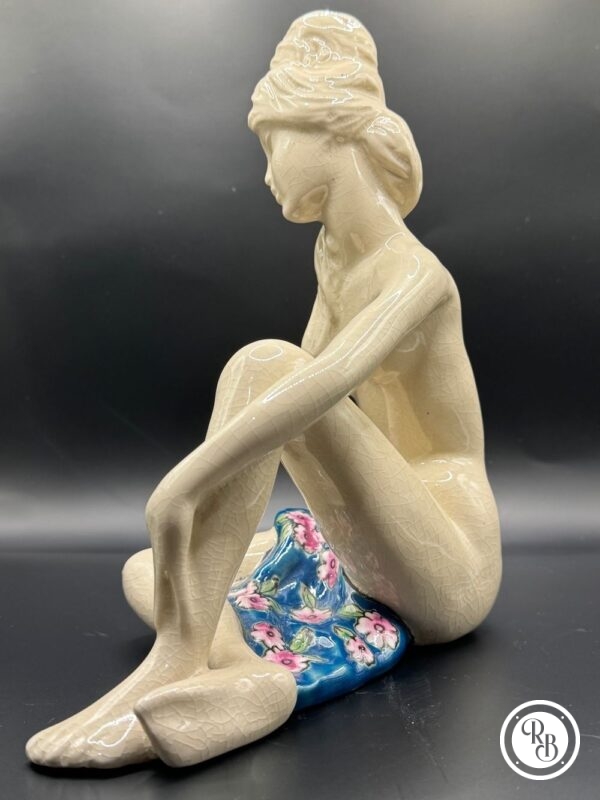 Sujet en céramique craquelée et émaillée figurant une jeune femme nue et assise, partiellement couverte d'une serviette à décor de fleurs polychromes