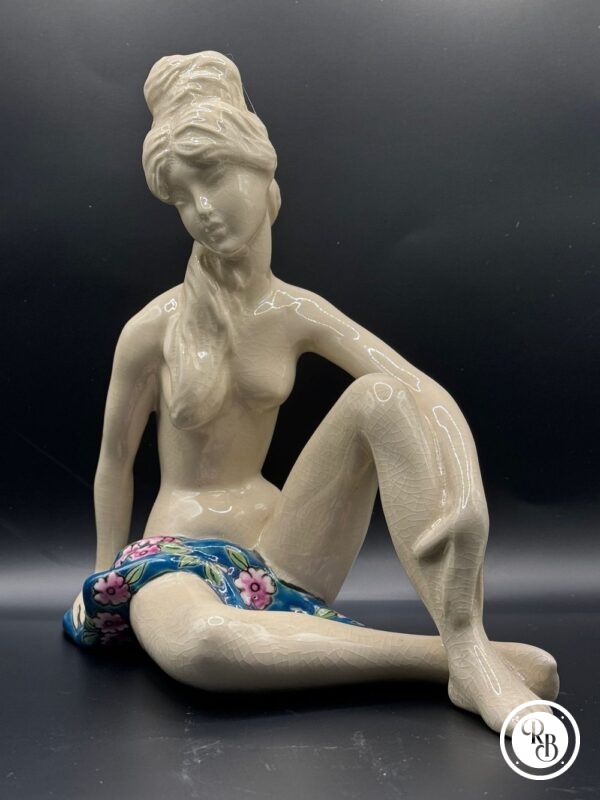 Sujet en céramique craquelée et émaillée figurant une jeune femme nue et assise, partiellement couverte d'une serviette à décor de fleurs polychromes
